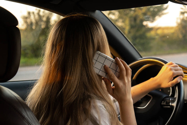 Glückliche junge Frau, die während der Autofahrt mit dem Handy spricht. Geschäftsfrau telefoniert im Auto. Unsicher riskantes Fahren. Konzept des Multitasking  - Foto, Bild