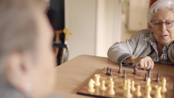 Slow motion video of two female senior friends playing chess in a nursing home - Footage, Video