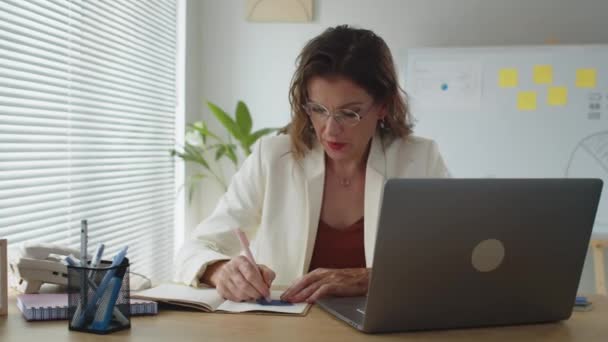 Portrait moyen de femme chef de produit écrivant des notes et souriant à la caméra au bureau - Séquence, vidéo
