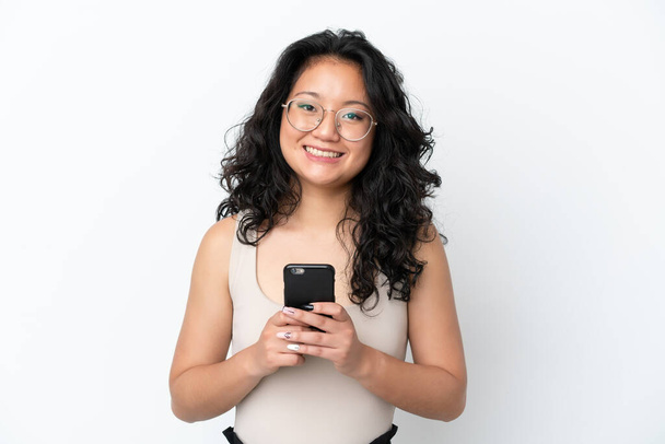 Jeune femme asiatique isolé sur fond blanc regardant la caméra et souriant tout en utilisant le mobile - Photo, image