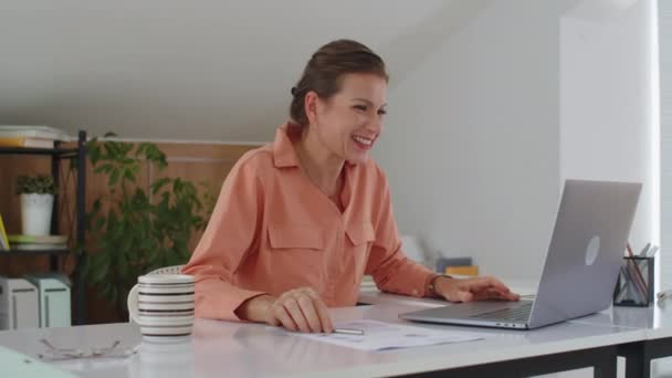 Medium shot van middelbare leeftijd Kaukasische vrouw verheugen zich op de bevordering van de werkgelegenheid zittend in de voorkant van laptop op kantoor - Video