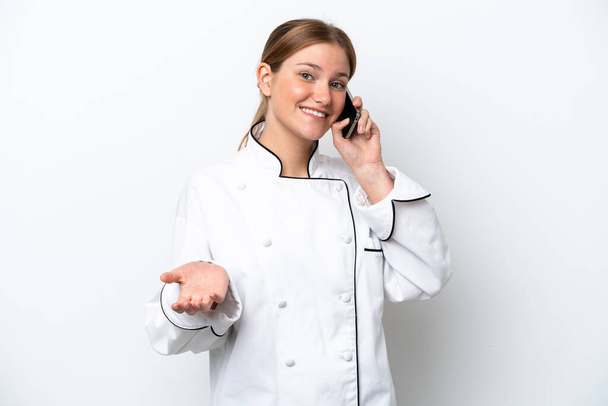 Young chef woman isolated on white background keeping a conversation with the mobile phone with someone - Photo, Image