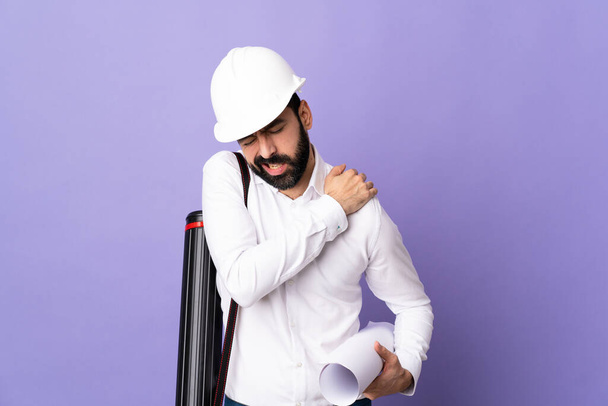 Młody architekt w kasku trzymający plany na odizolowanym fioletowym tle cierpiący na ból w ramieniu za wysiłek - Zdjęcie, obraz