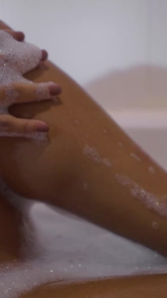 Manos de mujer acarician sus piernas en una bañera de espuma - FHD Vídeo vertical - Metraje, vídeo