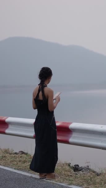 Девушка смотрит на свой мобильный телефон перед потрясающим горным озером - 4K Горизонтальный образ жизни видео - Кадры, видео