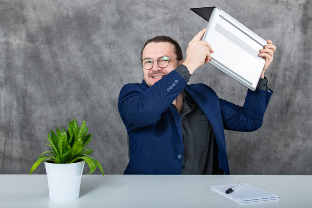 Un professionnel des affaires concentré dans un costume bleu à la mode travaille sur un ordinateur portable dans un espace de bureau moderne, avec une plante verte dynamique offrant une touche de nature en arrière-plan. - Photo, image