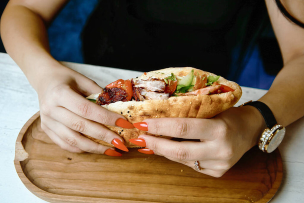 Женщина держит в руках сэндвич, демонстрируя вкусную еду, которой она собирается насладиться. - Фото, изображение