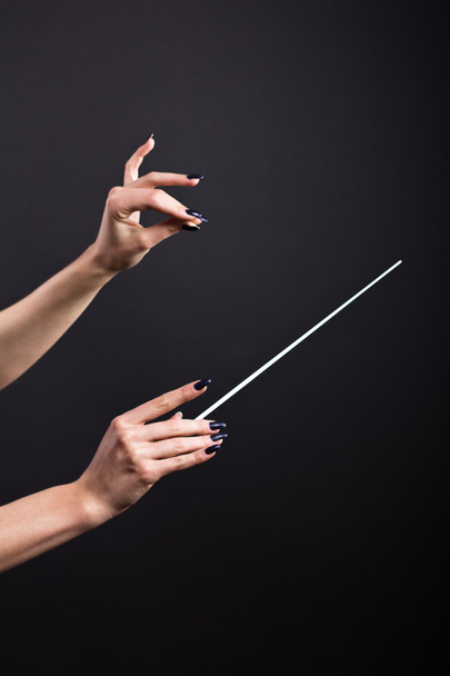 Dirigentenstab in schönen Frauenhänden auf schwarzem Hintergrund. Dirigentenstab im Dunkeln. - Foto, Bild