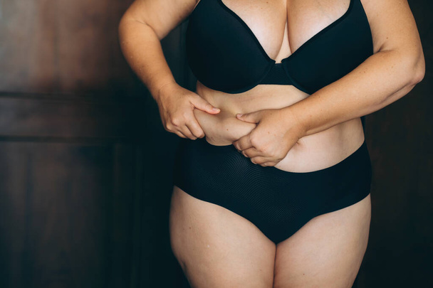 Жінка стискає жир живота, спільне занепокоєння зображенням тіла та здоров'ям, в момент усвідомлення особистого тіла. - Фото, зображення