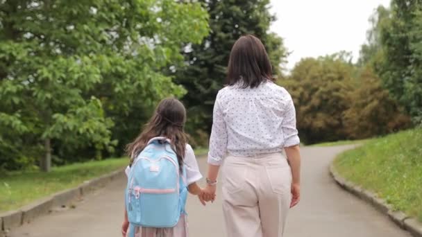 Anya és lánya sétálnak az aszfalt ösvényen a parkban, kéz a kézben. Élvezik a közös nyaralást a természetben.. - Felvétel, videó