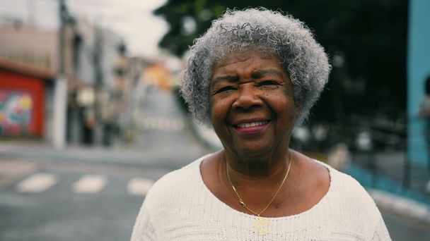 Una mujer mayor negro feliz caminando hacia adelante a la cámara en stret entorno urbano. Cabello gris anciana dama sudamericana en los años 80 que representa la vejez madura activa, retrato de cerca - Foto, imagen