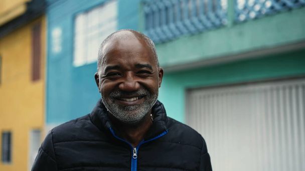 Güney Amerikalı neşeli bir siyah adam şehir sokağında kameraya gülümsüyor, yakın plan çekimde ve şehir planında - Fotoğraf, Görsel