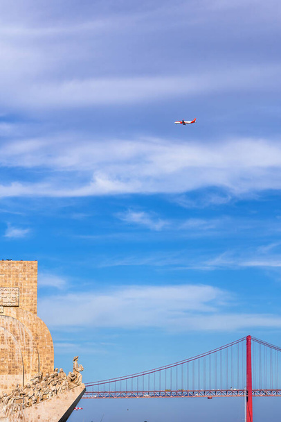 Profil ouest du monument aux découvertes, avec des touristes sur le grenier regardant le pont 25 de Abril et un avion de ligne commercial volant dans le ciel. - Photo, image