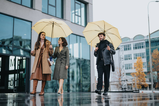 Socios de negocios modernos caminando con sombrillas en la calle de la ciudad lluviosa. - Foto, imagen