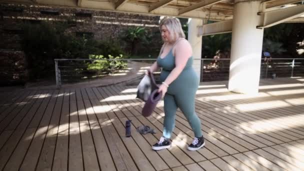 Une femme range après une séance de yoga gratifiante à l'extérieur, roulant son tapis sur une terrasse en bois. - Séquence, vidéo