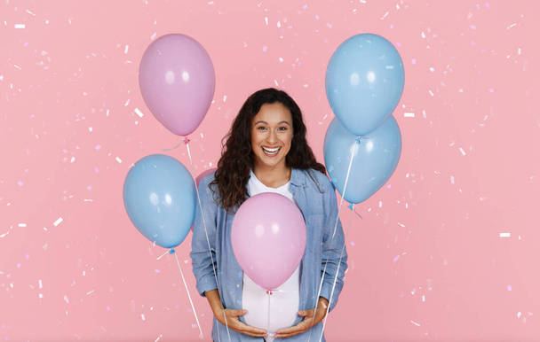 誕生日のお祝い 性別がパーティーを明らかにする。 ピンクのスタジオの背景に美しいシャワーの下に立っているカラフルなピンクとブルーの風船を持つ幸せな美しい美しい若い妊娠中の女性 - 写真・画像