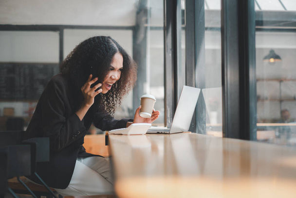 Geschäfts- und Technologiekonzept, Eine lächelnde junge Frau in lässiger Businesskleidung führt ein Gespräch auf ihrem Mobiltelefon, während sie im Büro eine Kaffeetasse hält. - Foto, Bild