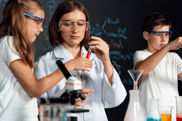 Lehrer unterstützen die Schüler und beobachten sie im Labor, tragen Schutzbrillen, stehen auf und experimentieren im MINT-Unterricht über Chemie. Schüler experimentieren lustigerweise mit Flüssigkeit im Schlauch. Erution. - Foto, Bild