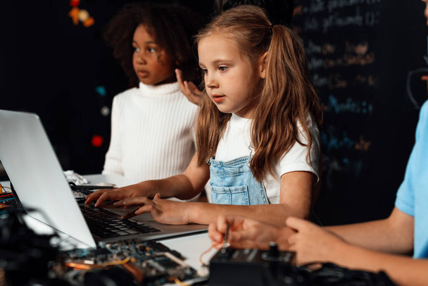 Beyaz önlüklü akıllı kız BTMM sınıfında dizüstü bilgisayar kullanarak robotik teknolojiyi öğreniyor. Mavi tişörtlü öğrenci anakart öğretirken zeki öğrenciler kod okumaya çalışıyor. Etkinlik. - Fotoğraf, Görsel