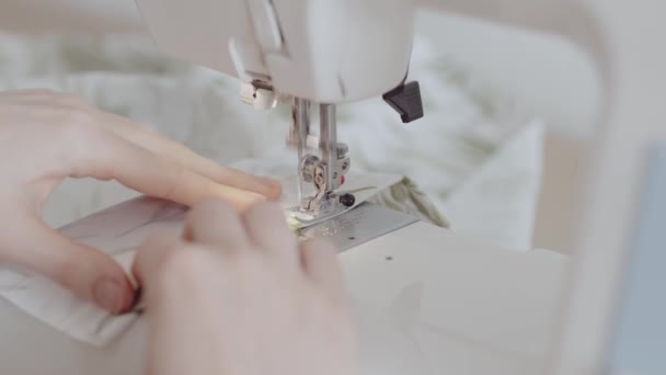 Primer plano de una tela de coser de manos de mujer con una máquina de coser en un entorno de taller ligero. - Metraje, vídeo