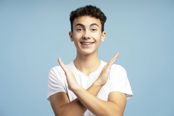 Excited, smiling boy wearing white t shirt showing his arms crossed, looking at camera. Attractive teenager gesturing no sign. Forbidden concept - Photo, Image