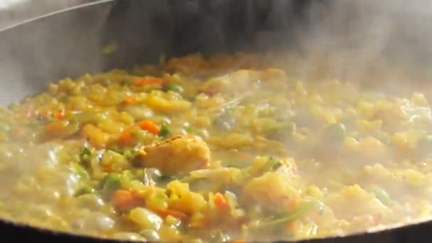Velká pánev bublajícího rizota se vaří. Rizoto se zeleninou a kousky kuřete se připravuje v domácí kuchyni zblízka. - Záběry, video