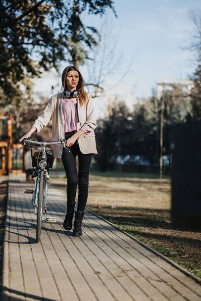 Jovem elegante com sua bicicleta em um dia ensolarado no parque, apresentando um estilo de vida urbano e transporte ecológico. - Foto, Imagem