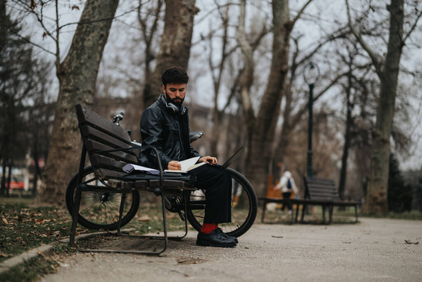 スタイリッシュなビジネスマンは静かな公園のベンチに座っている間レポートを読むことに焦点を当て,モバイル作業を例示しました. - 写真・画像