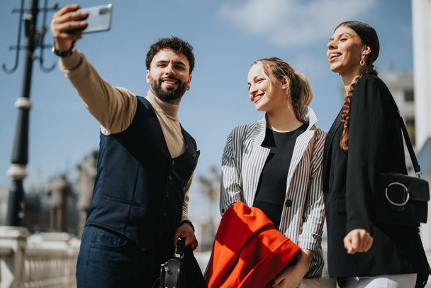 Young business associates enjoy a light moment, taking a selfie on a sunny day while discussing trends and market strategies outdoors. - Photo, Image