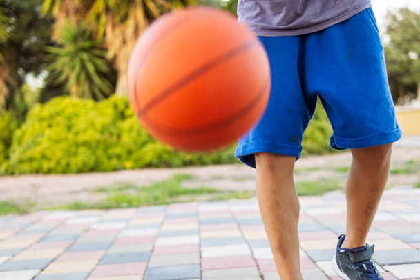 Um menino joga basquete no parque, close-up em seus pés e a bola, capturando a essência dos esportes ao ar livre e energia juvenil. - Foto, Imagem