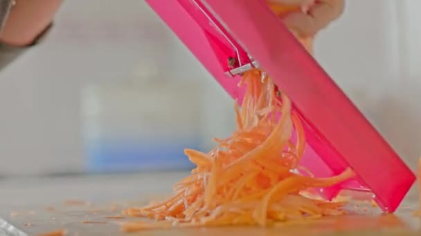 жіночі руки натирають моркву на червоній решітці за кухонним столом. - Кадри, відео