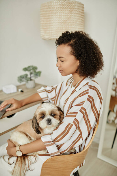 Minimales Porträt einer schwarzen jungen Frau, die es sich zu Hause gemütlich macht, mit Hund auf dem Schoß - Foto, Bild