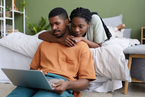 Afro-americanos encantadora pareja usando el ordenador portátil en fin de semana en casa mientras descansan en su dormitorio - Foto, Imagen