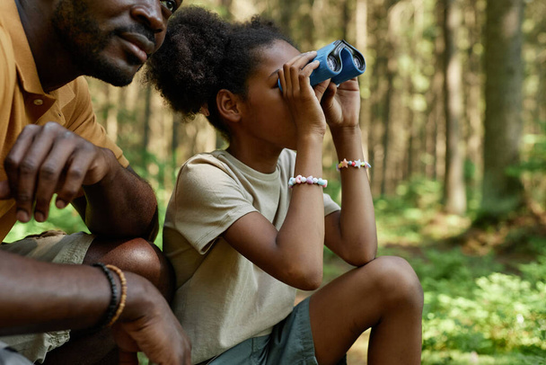 African American little girl looking through binoculars during hiking with her dad - Photo, Image