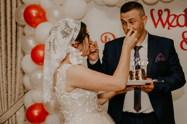 Ženich a nevěsta na svatbě nakrmili svou velkou, mnohovrstevnou chuť bílého dortu. Slovanské ukrajinské ruské tradice - Fotografie, Obrázek