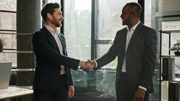 Diverse multiracial African American and Caucasian colleagues businessmen business coworkers men talking in office shake hands. Man leader recruiter hiring manager to work handshaking agreement deal - Photo, Image
