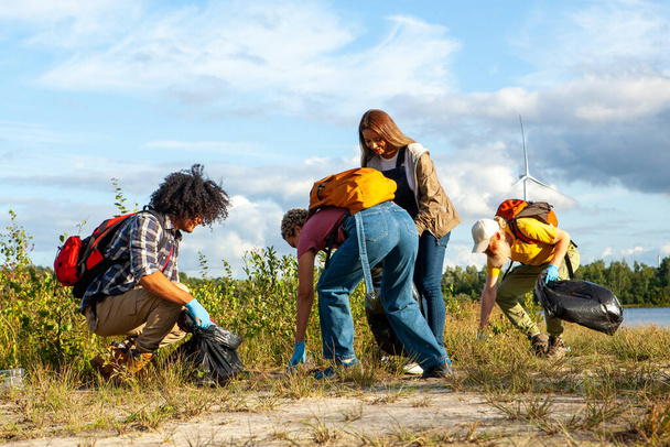 This inspiring image captures a group of environmentally conscious friends, from diverse ethnic backgrounds including Caucasian and Black, participating in a lakeside cleanup. Each person is actively - Photo, Image