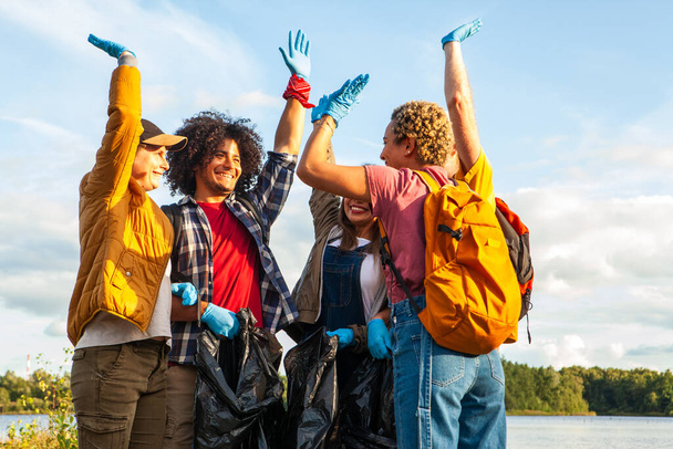 Gioioso gruppo di volontari alzando le mani in trionfo dopo uno sforzo di pulizia riva del lago. Volontari estatici Celebrare una pulizia del lago di successo. Foto di alta qualità - Foto, immagini