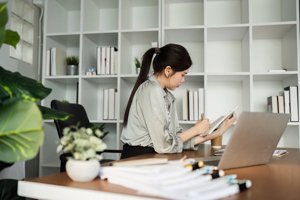 zakenvrouw werken met laptop tijdens het raadplegen van een aantal factuur en document in de werkruimte thuis. - Foto, afbeelding