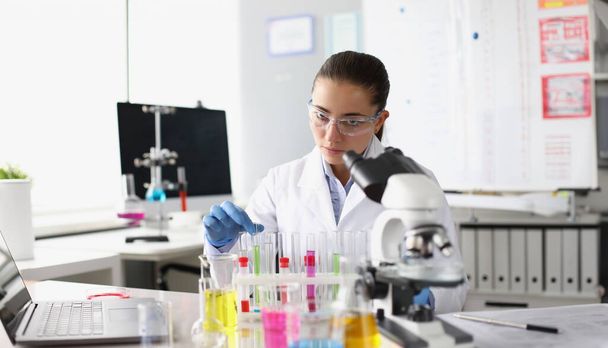 実験室で顕微鏡の前で液体で試験管を保持する化学女性。製薬業界のコンセプト - 写真・画像