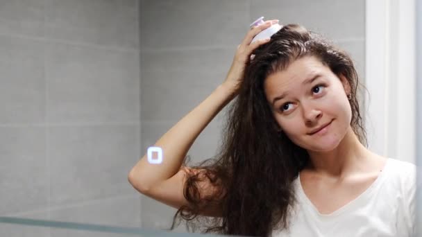 ダークカーリーヘアを持つ若い女性は,自宅のバスルームで刺激的な髪の成長のための頭皮マッサージや髪の成長のためのヘアブラシでセルフヘアスカルプマッサージを行っています. 鏡の視点を反映した. 高品質の写真 - 映像、動画