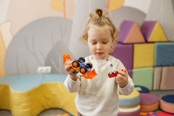 Skupiona dziewczynka bawi się kolorowymi zabawkami w żywym, zabawnym przedszkolu.. - Zdjęcie, obraz