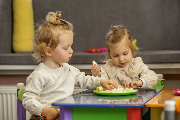 Двоє малюків діляться закускою на барвистому ігровому столі, беручи участь у соціальній та навчальній діяльності разом. - Фото, зображення
