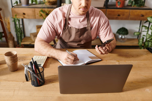 Ένας άνθρωπος κάθεται σε ένα τραπέζι με ένα σημειωματάριο και στυλό, ιδέες brainstorming για την επιχείρησή του κατάστημα φυτών. - Φωτογραφία, εικόνα