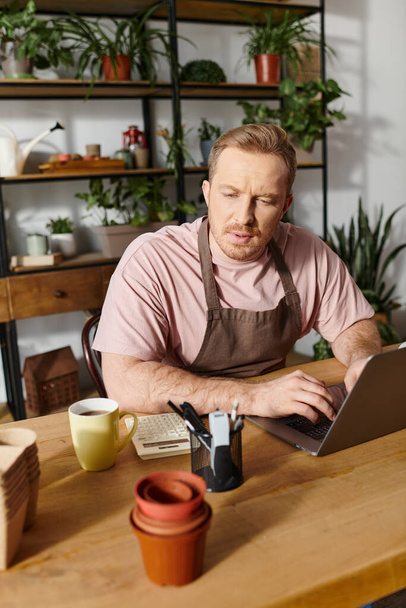 Egy férfi ül egy asztalnál egy gyárban, a laptopjára koncentrál, megtestesítve egy sikeres virágüzlet tulajdonosát.. - Fotó, kép