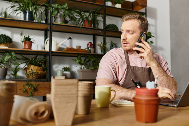 Muž sedí u stolu v květinářství, zabraný do hovoru na mobilu, a ztělesňuje malého podnikatele v akci. - Fotografie, Obrázek