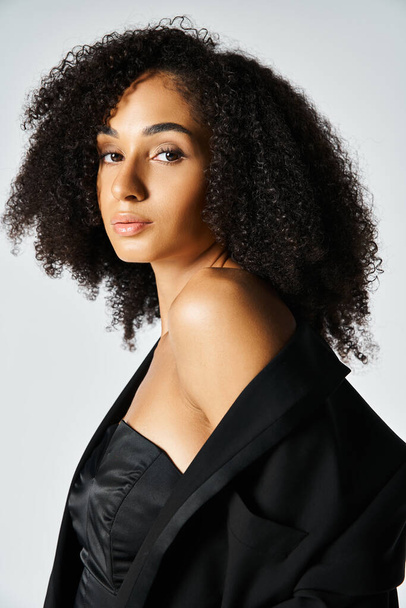 Egy fiatal afro-amerikai nő harisnyanadrágban magabiztos pózt üt, bemutatja szépségét egy stúdióban, szürke háttérrel.. - Fotó, kép
