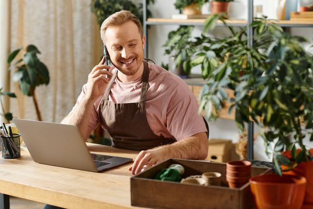 Um homem, dono de uma loja de plantas, conduz negócios em um telefone celular em sua mesa com determinação. - Foto, Imagem