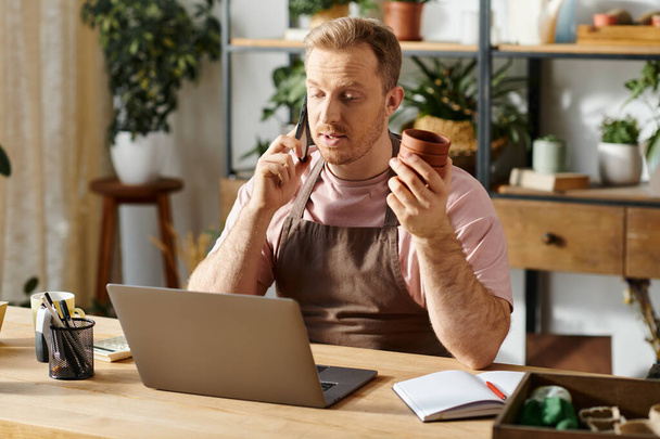 Człowiek z laptopem siedzący przy stole w zakładzie, prezentujący istotę własności małego biznesu i przedsiębiorczości. - Zdjęcie, obraz