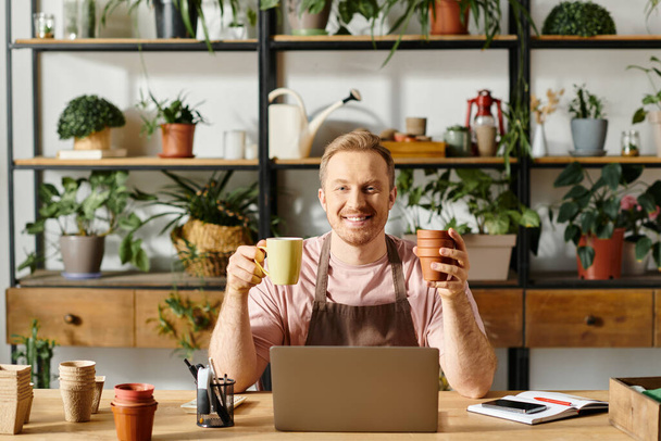 Человек сидит за столом, держа чашку и горшок в веселой манере - Фото, изображение